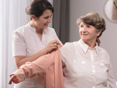 caregiver assisting elder woman on wearing a shirt