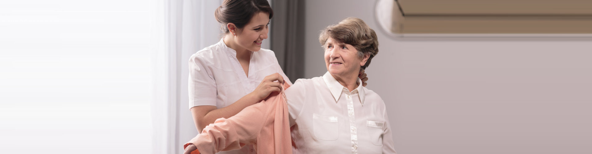 caregiver assisting elder woman on wearing a shirt